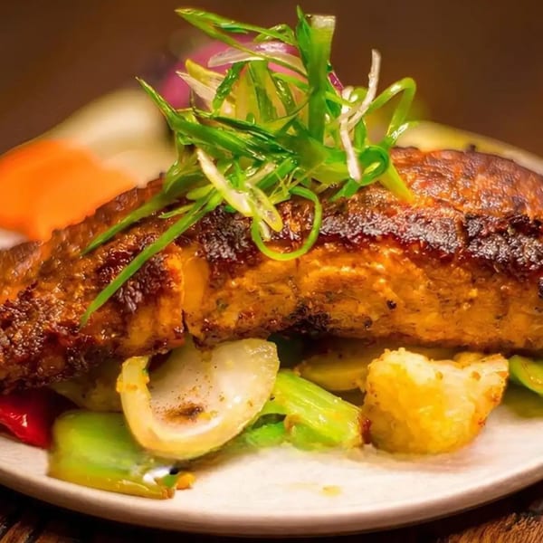 Grilled fish fillet topped with green onions, served with roasted vegetables on a white plate.
