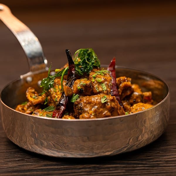 Spicy Indian curry with dried red chilies and fresh cilantro in a hammered metal serving dish.