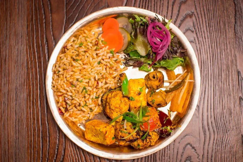 A vibrant Indian thali with rice, paneer tikka, vegetables, and a fresh salad on a wooden table.