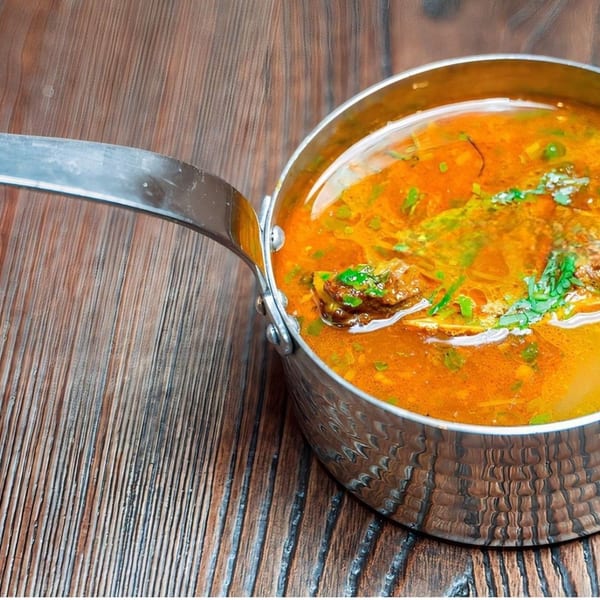 Hearty orange stew with meat and green herbs in a metal pot on a wooden table.