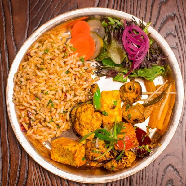 Overhead view of a silver platter with rice, salad, paneer, and various grilled vegetables.