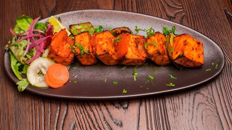 Grilled paneer tikka with green peppers, lime, and a side salad on a dark plate.