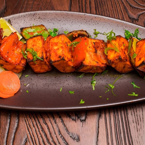 Grilled paneer tikka with bell peppers, onions, and a side salad on a dark plate.