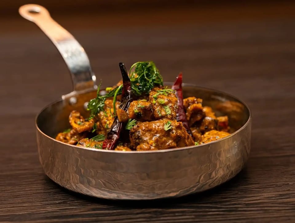 Spicy Indian chicken curry with herbs and dried chilies in a hammered metal pan.