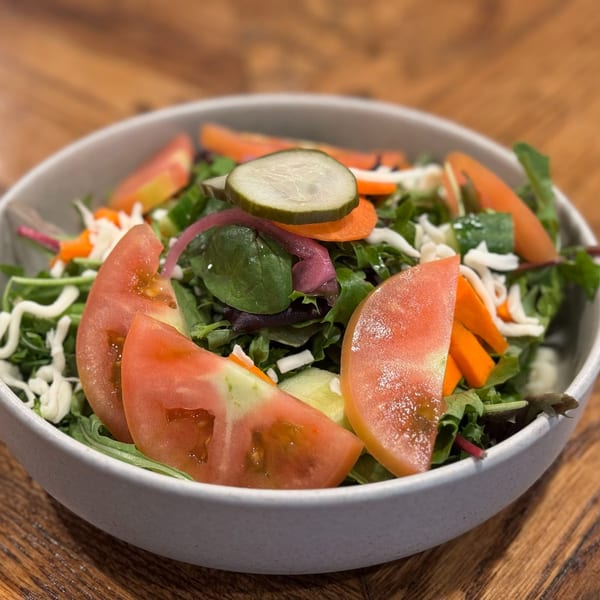 Fresh garden salad with mixed greens, tomatoes, carrots, pickles, and shredded cheese in a white bowl.