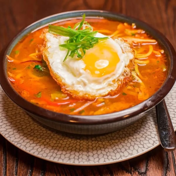 A bowl of ramen with a fried egg and green onions on top, served on a patterned plate.
