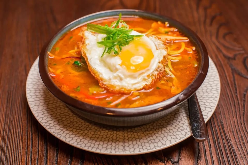 A bowl of ramen with a fried egg and green onions on top, served on a patterned plate.